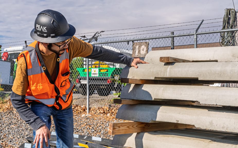 land-dev Worker inspects stacked concrete slabs outdoors.