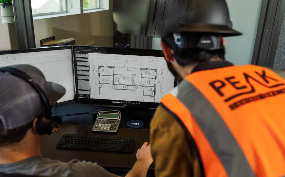 Workers reviewing architectural plans on computer monitors.