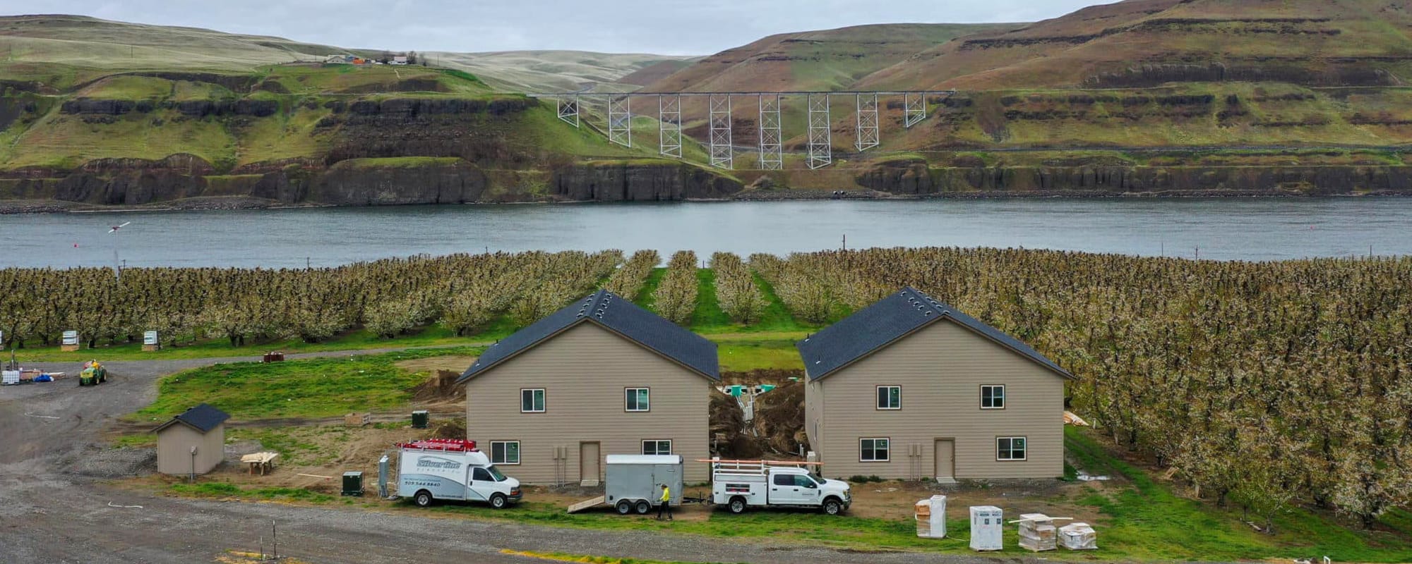 Orchard and houses by river, hills in background