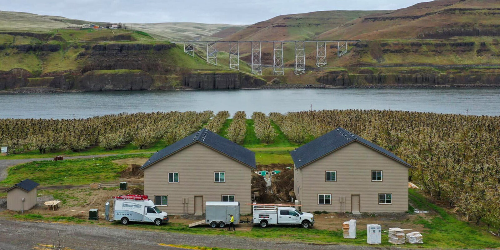 Orchard and houses by river, hills in background